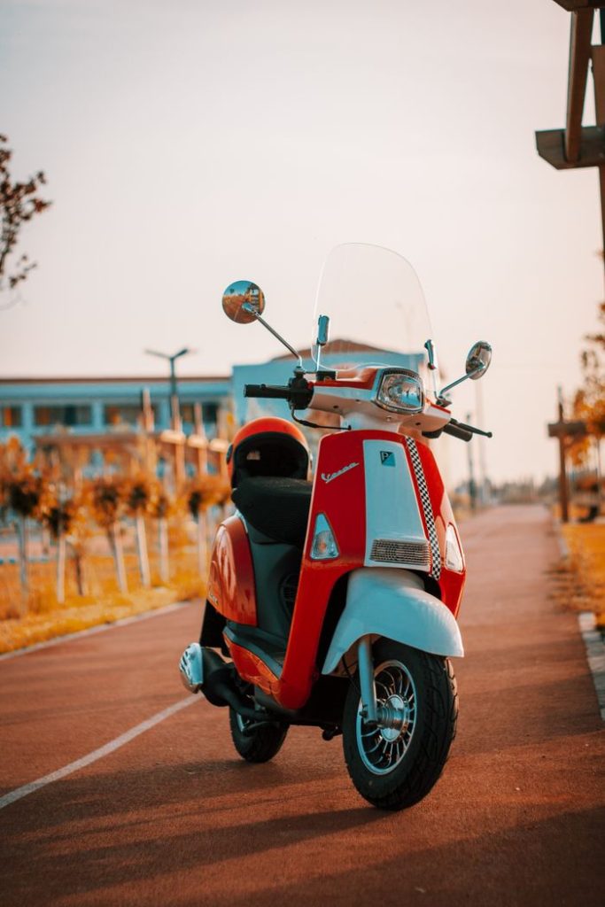 A bright red Vespa scooter parked on a picturesque path during sunset, surrounded by warm tones.